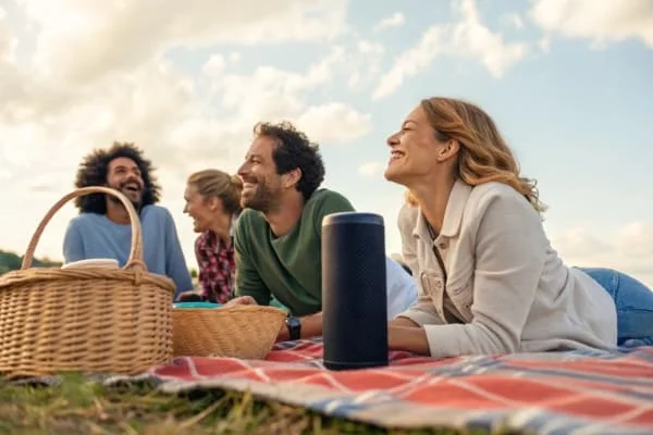 A group of friends listening to music from a Bluetooth speaker at a picnic