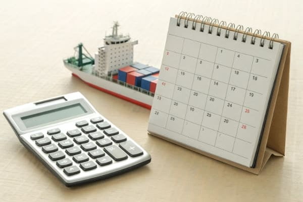 A calendar and a calculator next to a cargo ship to represent time and cost