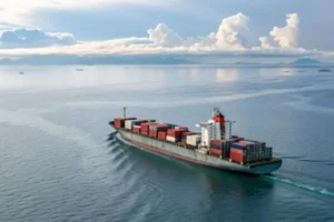 A large cargo ship carrying containers sails smoothly across a calm sea under a clear sky, highlighting international shipping.