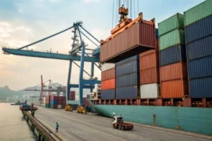 Shipping containers are lifted by a crane at a port, showcasing logistics and supply chain operations. A worker and truck are visible.