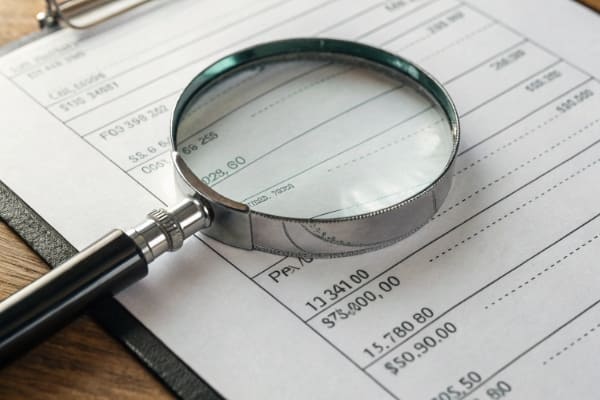 An invoice with a magnifying glass highlighting hidden fees in the fine print