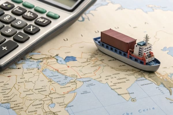 A calculator and a miniature container ship on a map between China and UAE