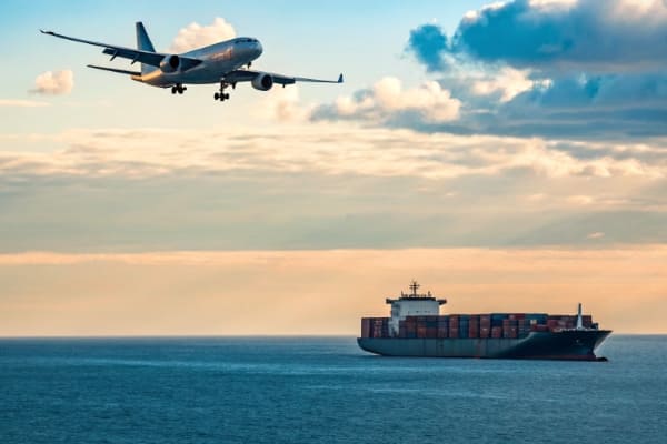 An airplane in the sky and a container ship on the sea